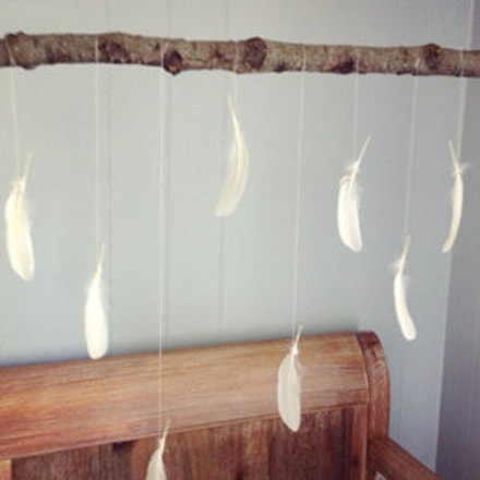 Customer appreciation photo of a baby feather mobile using white feathers from Running Bug Farm along with a rustic stick to hang.