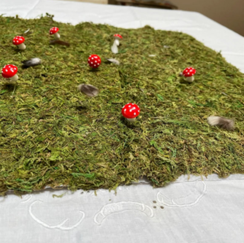 Happy customer photo review of their hand crafted Easter dinner table display. It features green moss, tiny red topped mushrooms and an assortment of miniature feathers from Running Bug Farm better than organic.