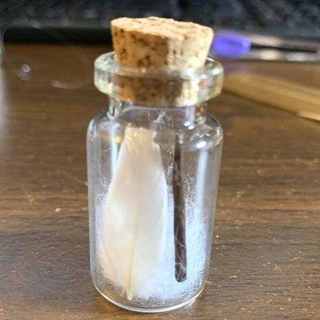 Happy customer picture of a miniature white feather & wand in a mini bottle for a Harry Potter spell (Wingardium Leviosa) fan recreation. Running Bug Farm